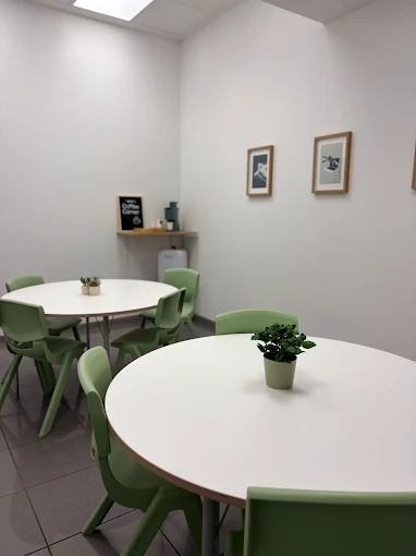 Sala de estudio con mesas redondas y sillas verdes en la academia A tu ritmo, Huesca